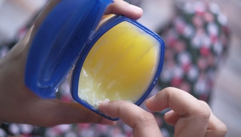 a person scooping vaseline from its original container using their index finger