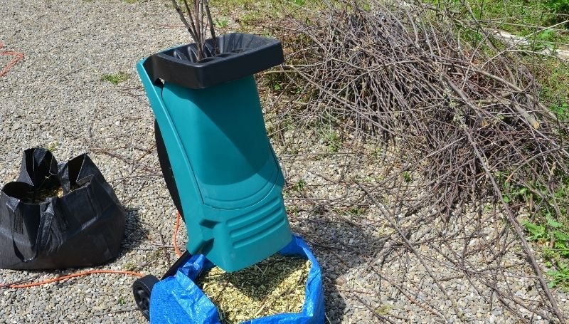 a blue wood chipper/shredder crushing dried twigs and branches