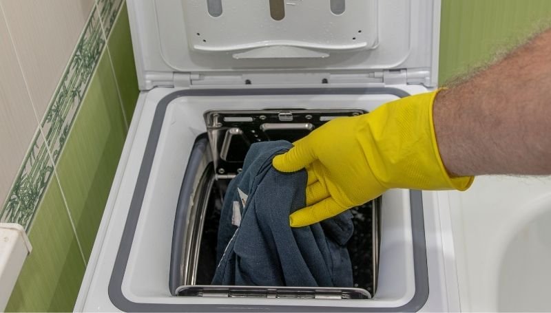 a guy in yellow latex gloves putting a piece of clothing in an off-grid washing machine
